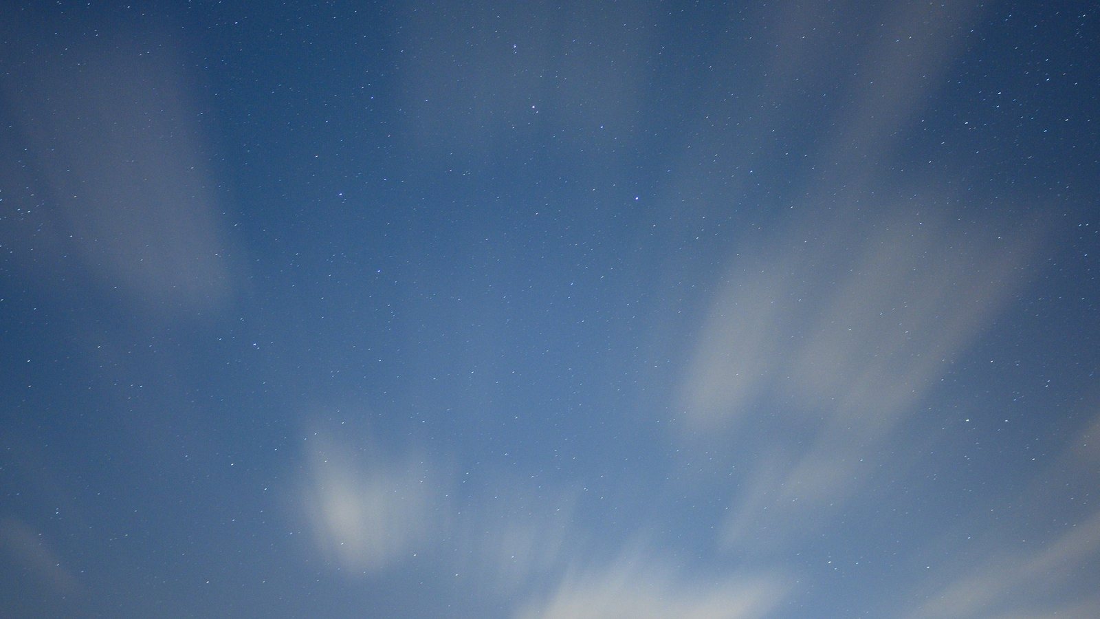 Ciel nocturne bleu profond parsemé d'étoiles et traversé de nuages fins et filants, sans horizon ni repère au sol
