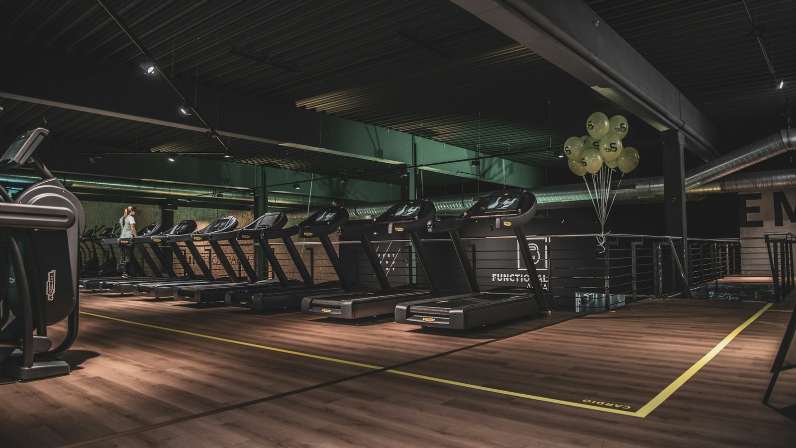 Rangée de tapis de course dans une salle de sport au sol en bois, éclairage tamisé