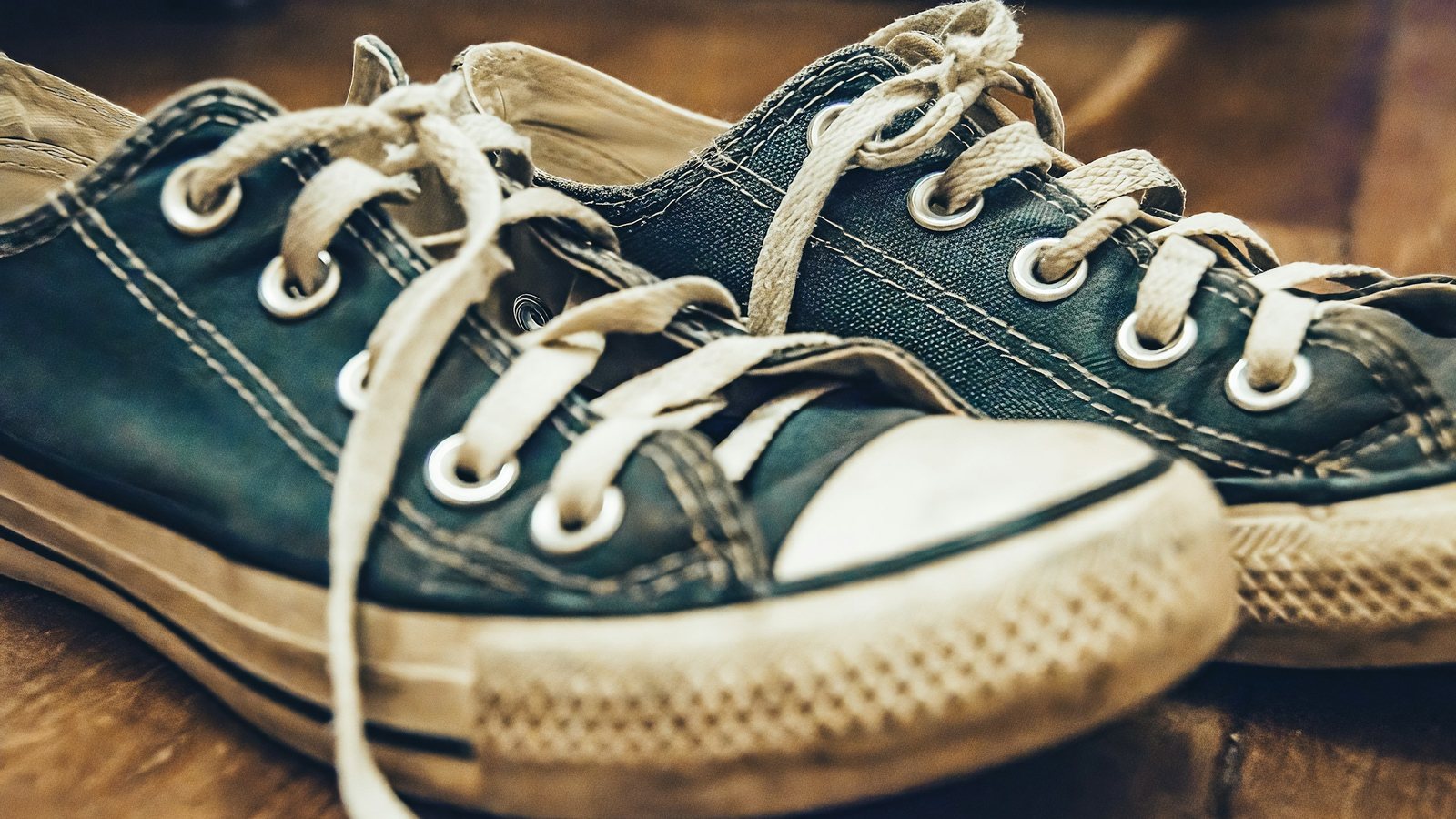 Paire de baskets en toile bleue usées, lacets défaits, posées sur un plancher