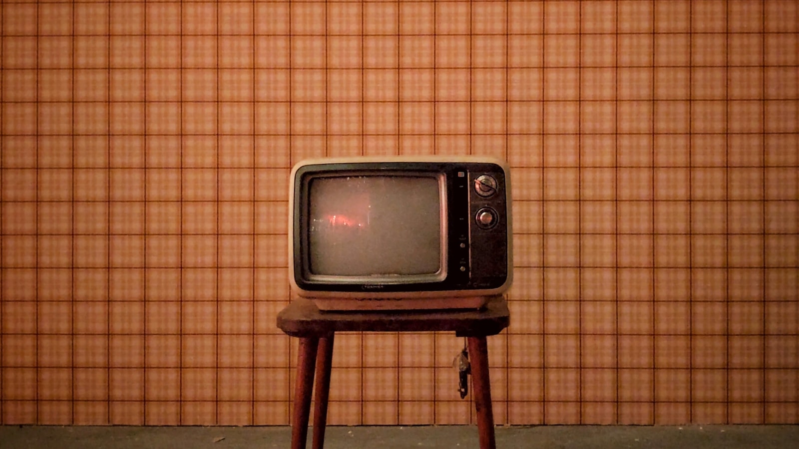 Téléviseur cathodique vintage devant un papier peint à carreaux
