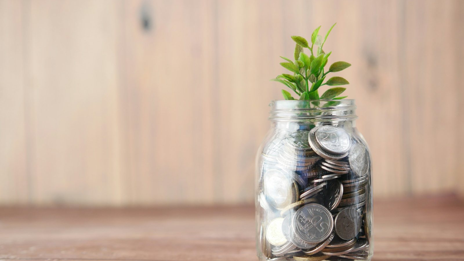 Bocal en verre rempli de pièces de monnaie posé sur une table en bois