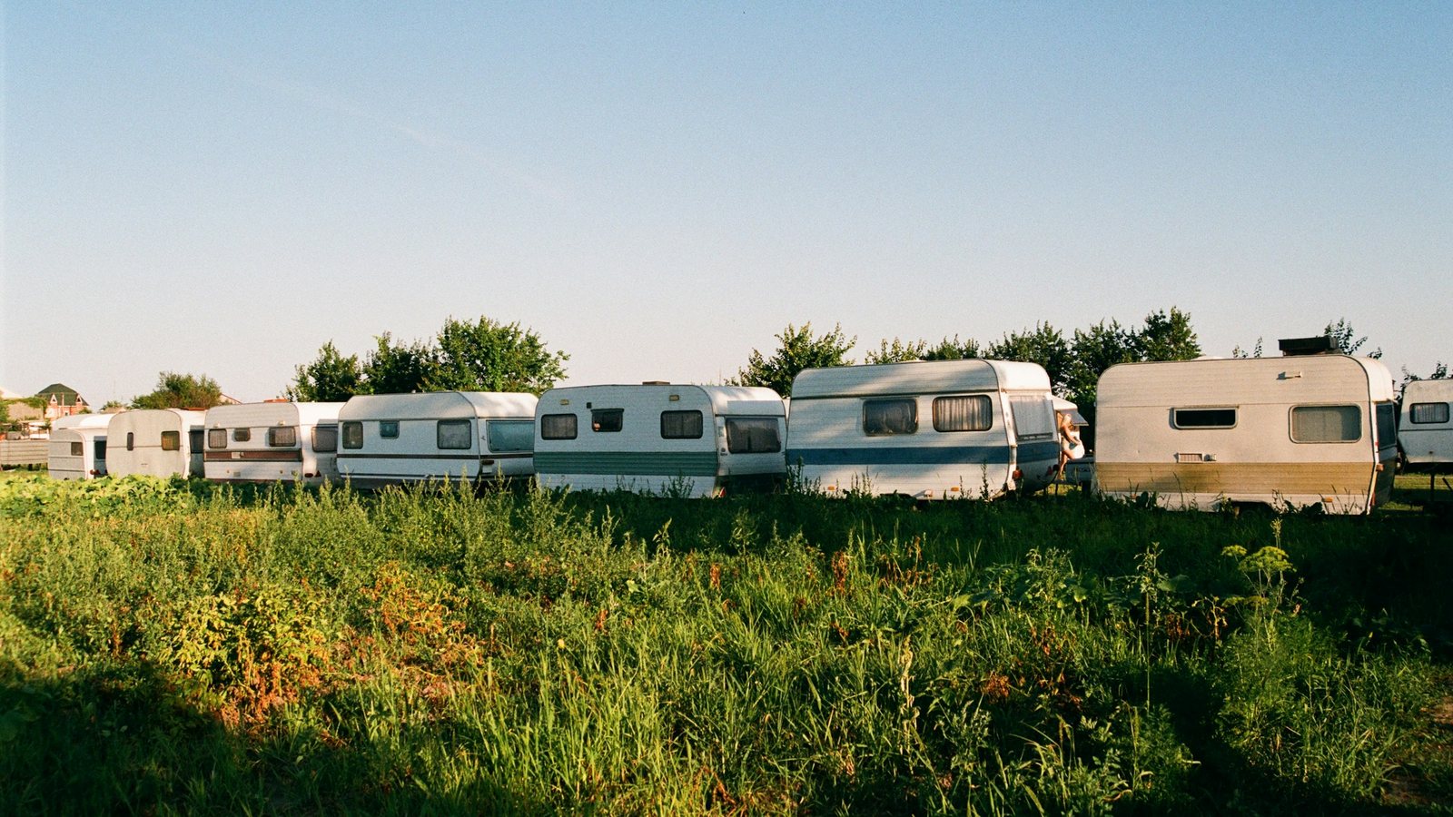 Rangée de caravanes blanches stationnées dans un pré, hautes herbes au premier plan