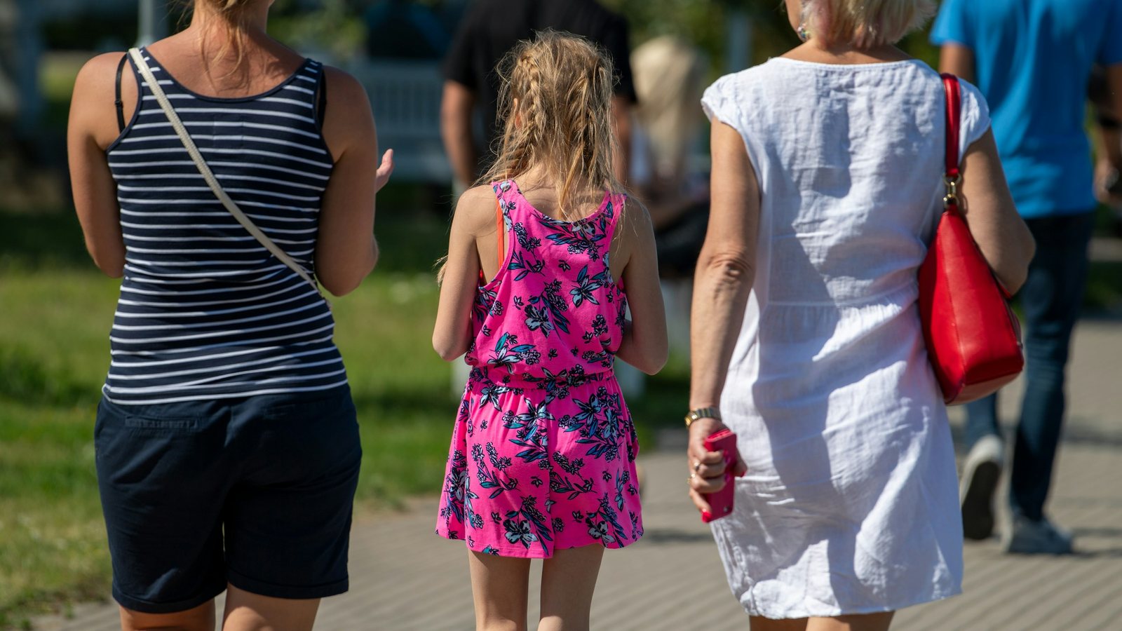 Deux adultes et une enfant marchant de dos sur une allée, visages invisibles