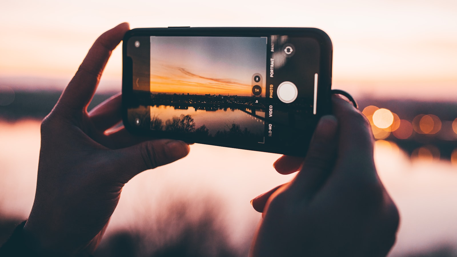 Main photographiant un coucher de soleil au smartphone