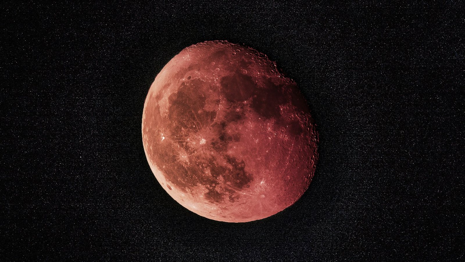 Gros plan de la Lune teintée de rouge cuivré sur un fond de ciel noir constellé d'étoiles, un bord assombri par l'ombre