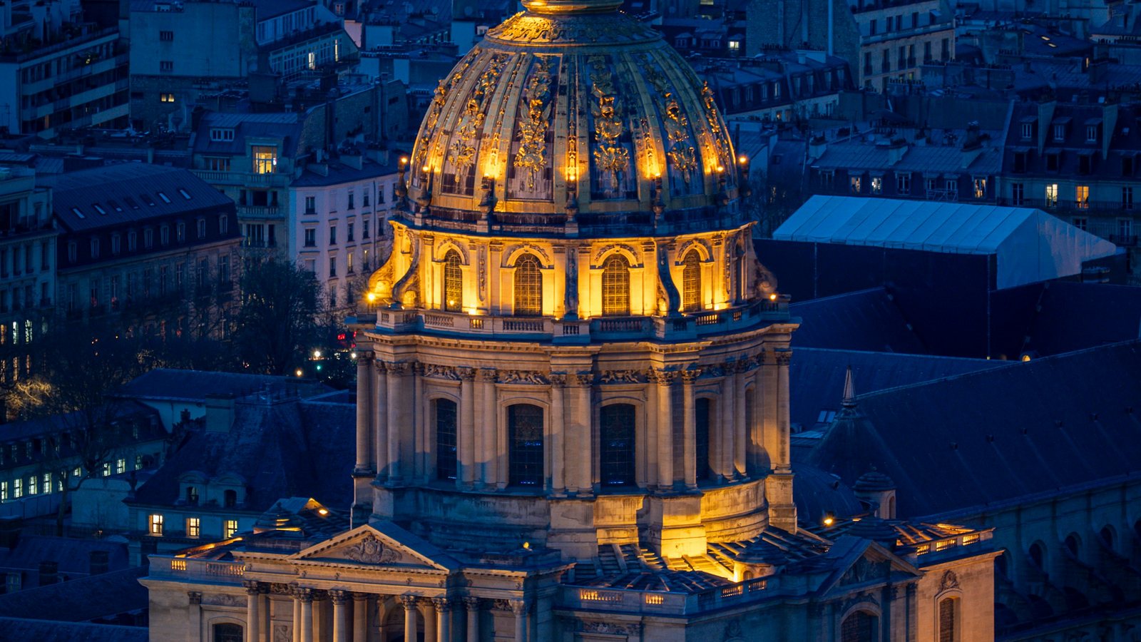Dôme doré d'un monument éclairé au-dessus de toits de ville serrés, dans le bleu profond du petit matin