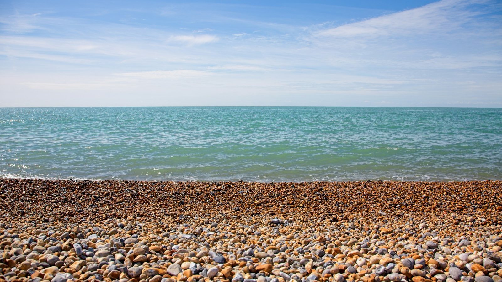 Plage de galets colorés devant une mer turquoise sous un ciel bleu