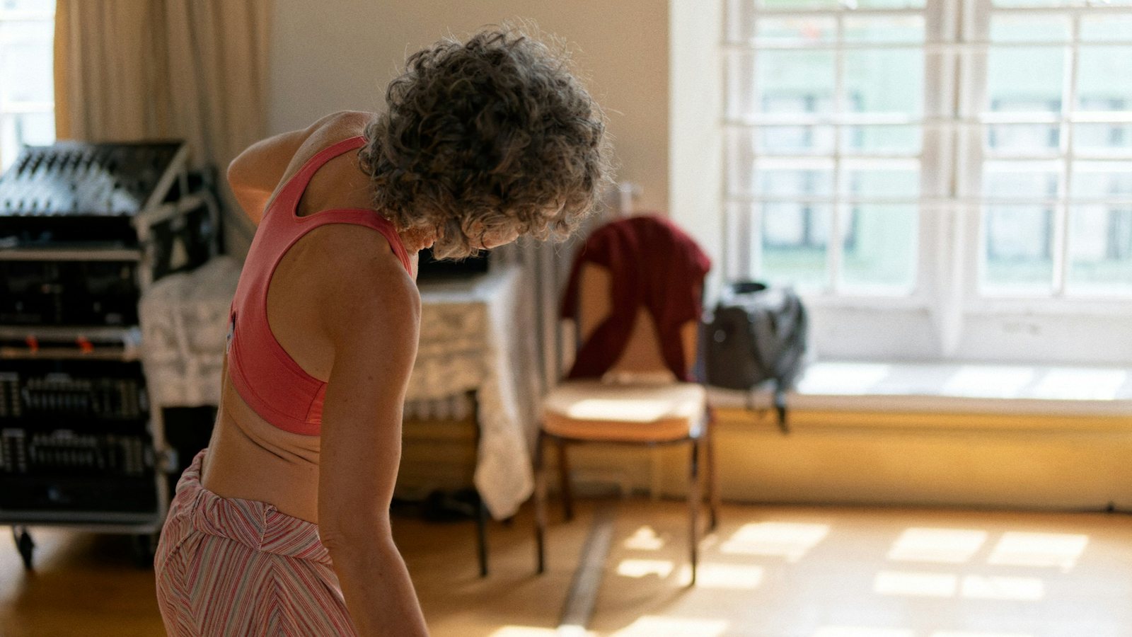 Femme aux cheveux gris en brassière de sport, vue de dos dans une pièce ensoleillée