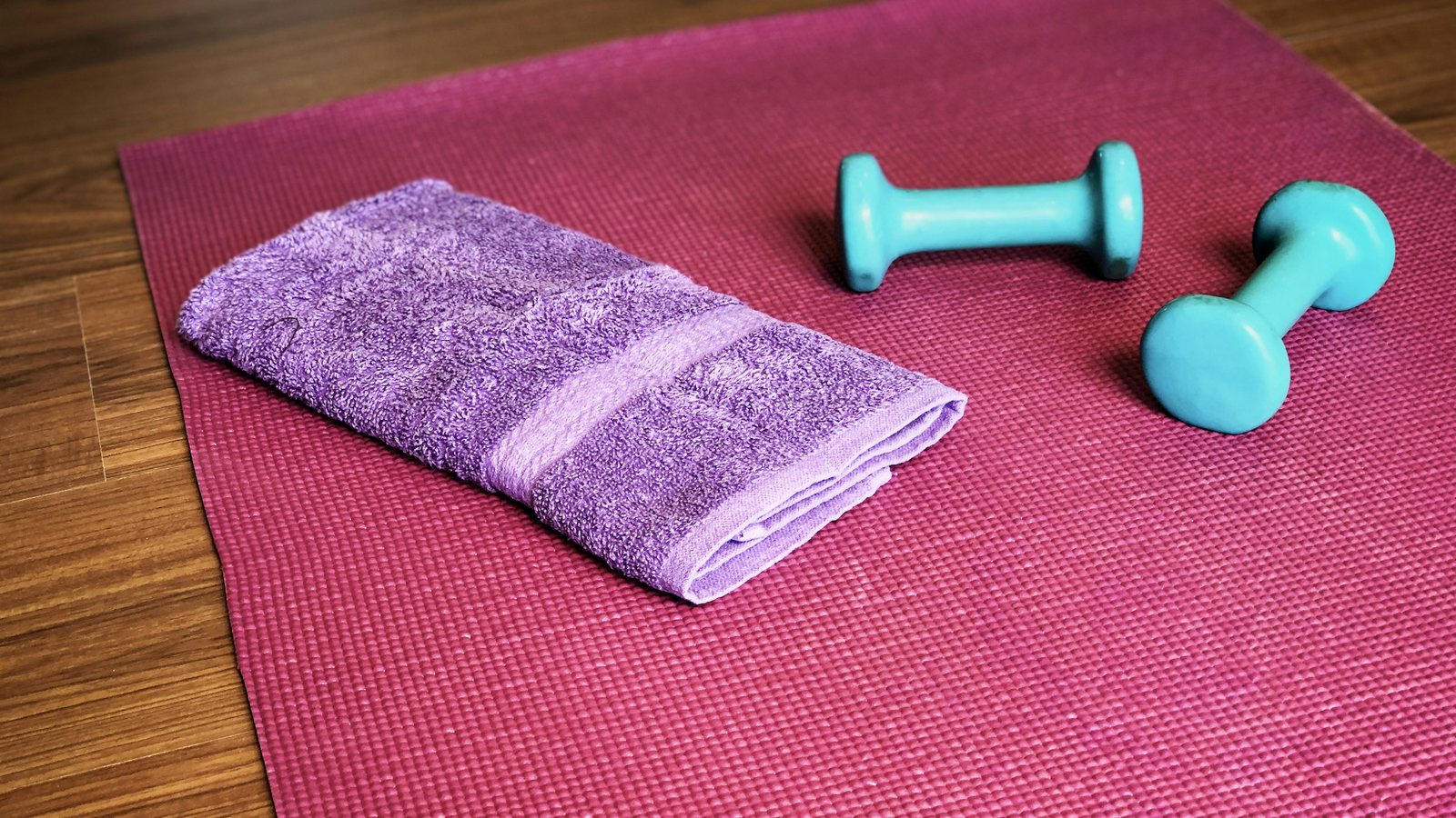 Tapis de yoga bordeaux déroulé sur un parquet avec serviette et deux haltères