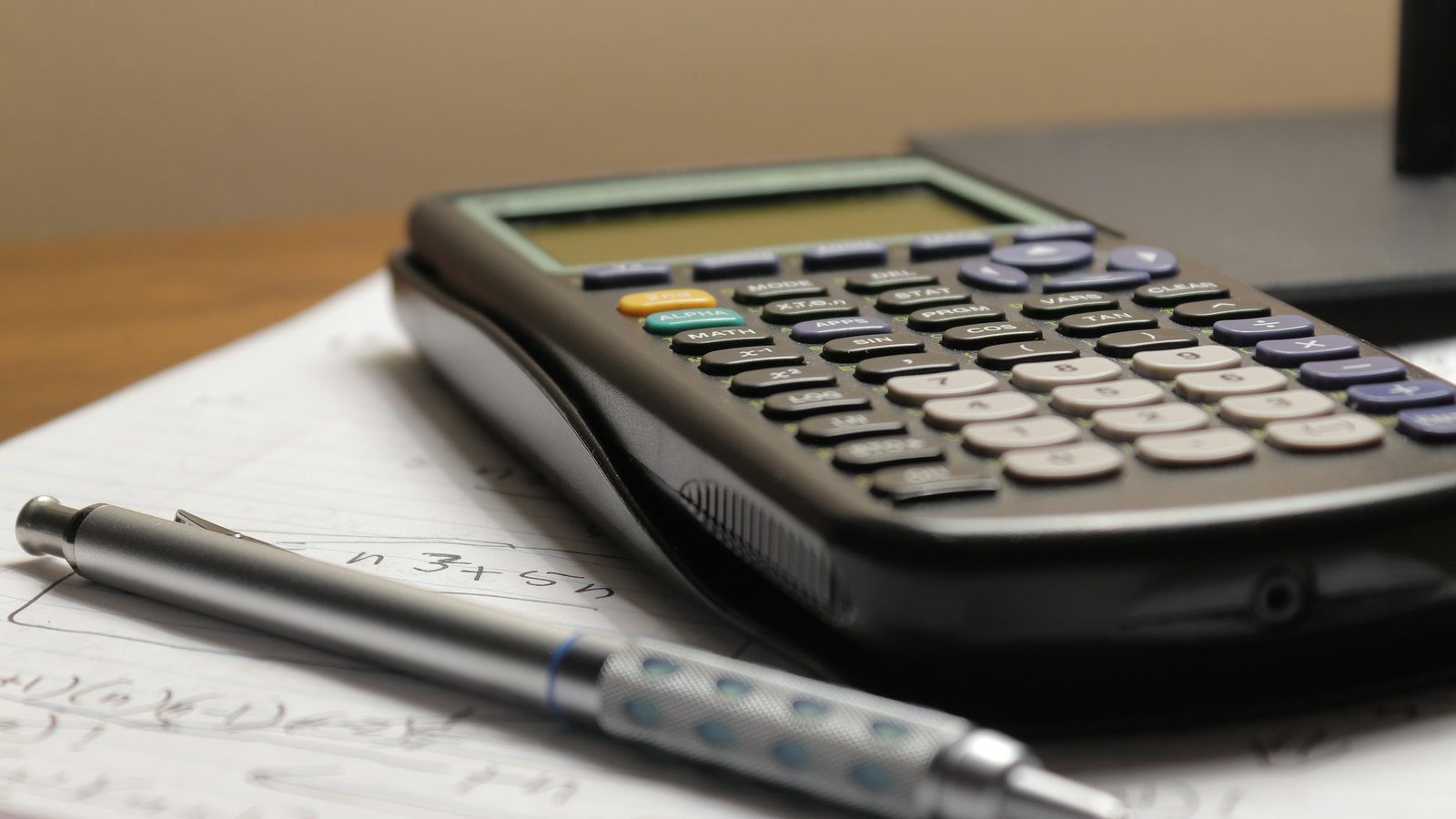Une calculatrice et un stylo posés sur des feuilles de calcul