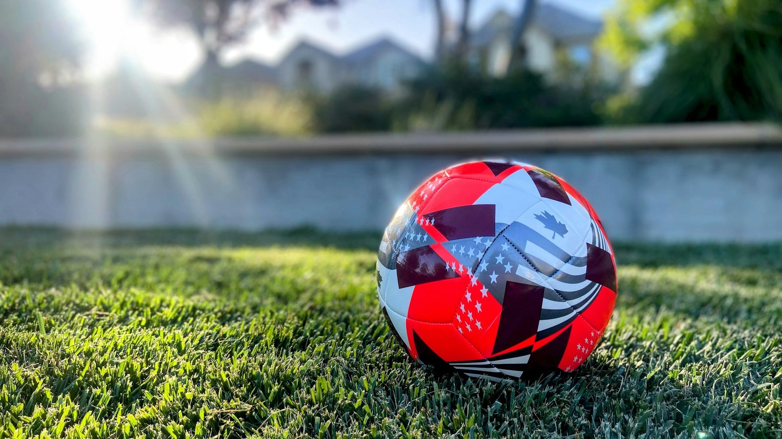 Ballon de football posé sur une pelouse verte, soleil rasant en arrière-plan