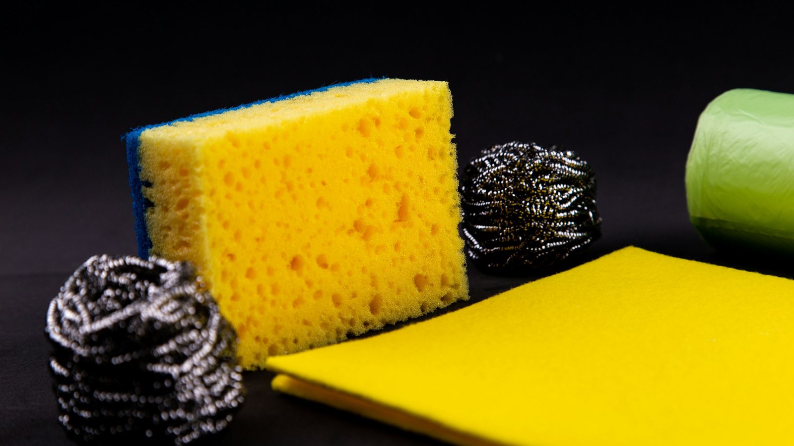 Éponge jaune, tampons métalliques, chiffon et savon sur fond noir