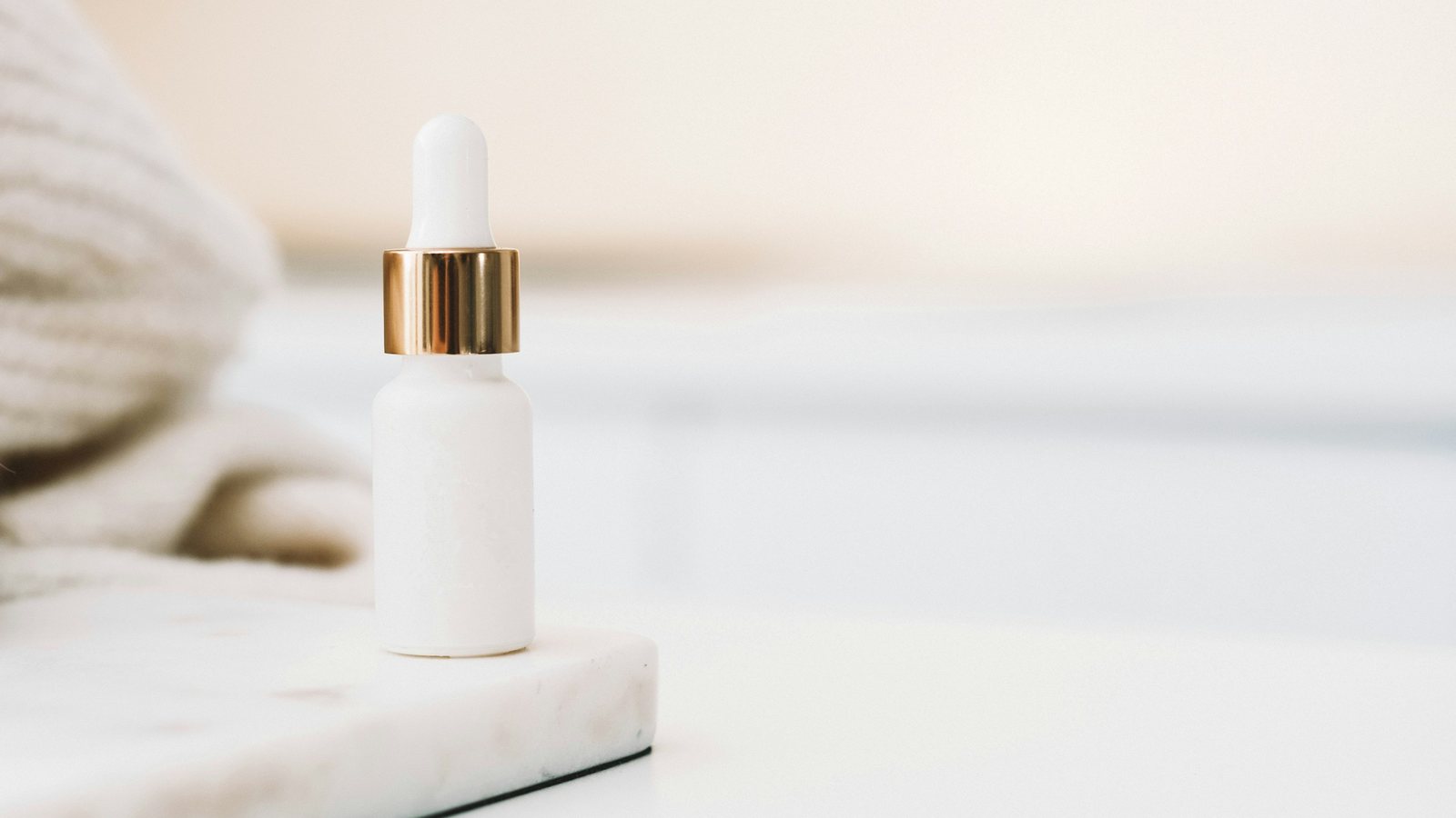 Flacon blanc de sérum cosmétique à pipette dorée posé sur un socle, fond clair