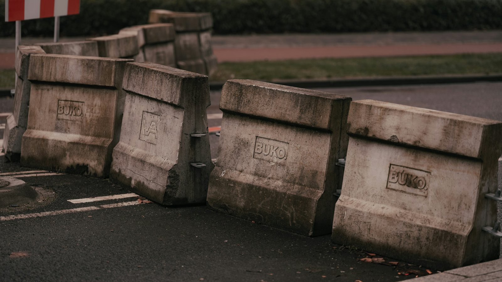 Rangée de blocs de béton gris barrant un accès, barrière rouge et blanche