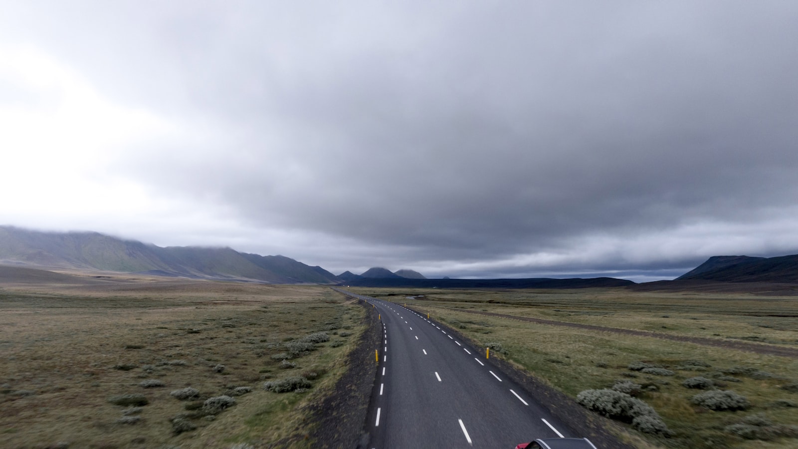 Sentier de montagne caillouteux serpentant sous un ciel changeant, avec des crêtes en arrière-plan