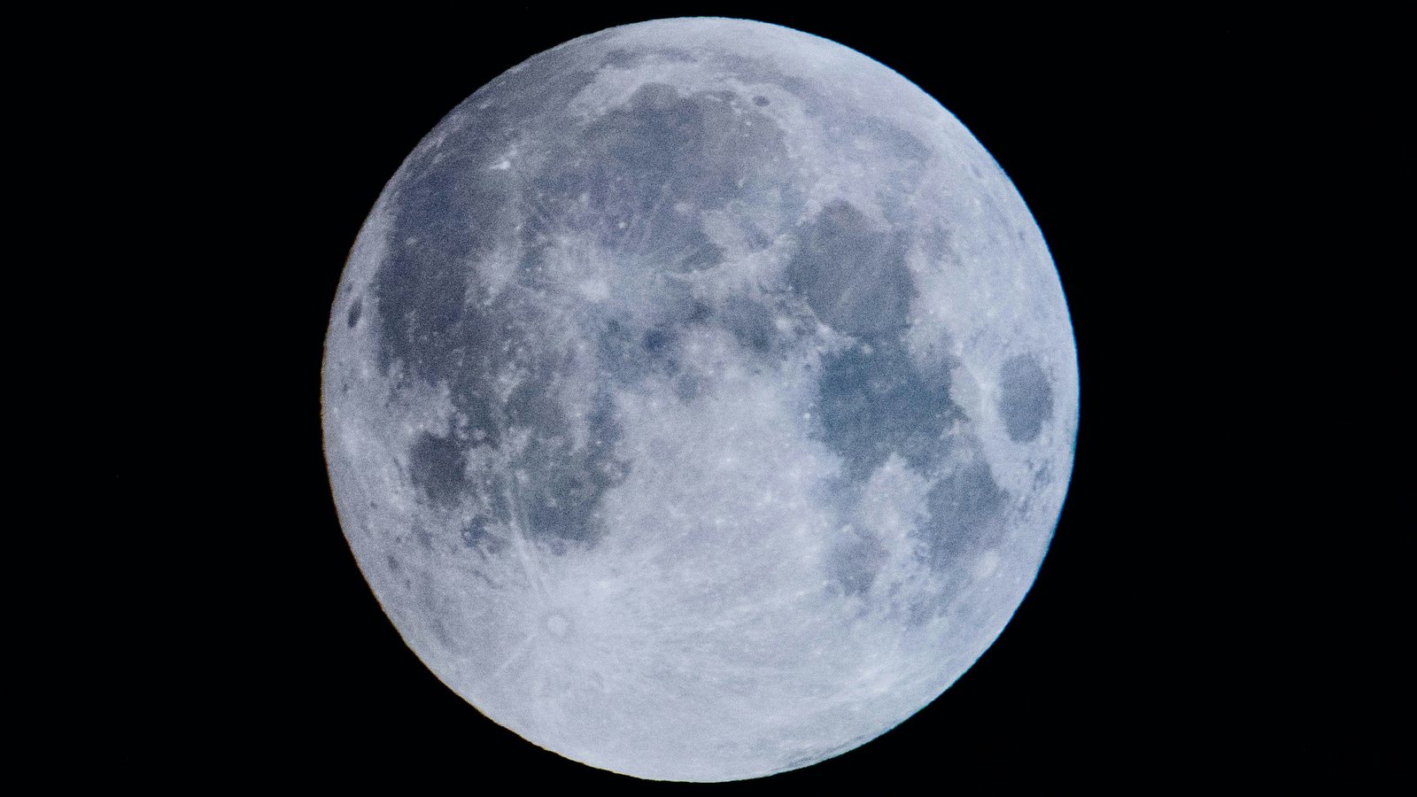 Gros plan au téléobjectif sur une Lune presque pleine aux teintes gris bleuté, ses mers sombres bien visibles, isolée sur un ciel noir