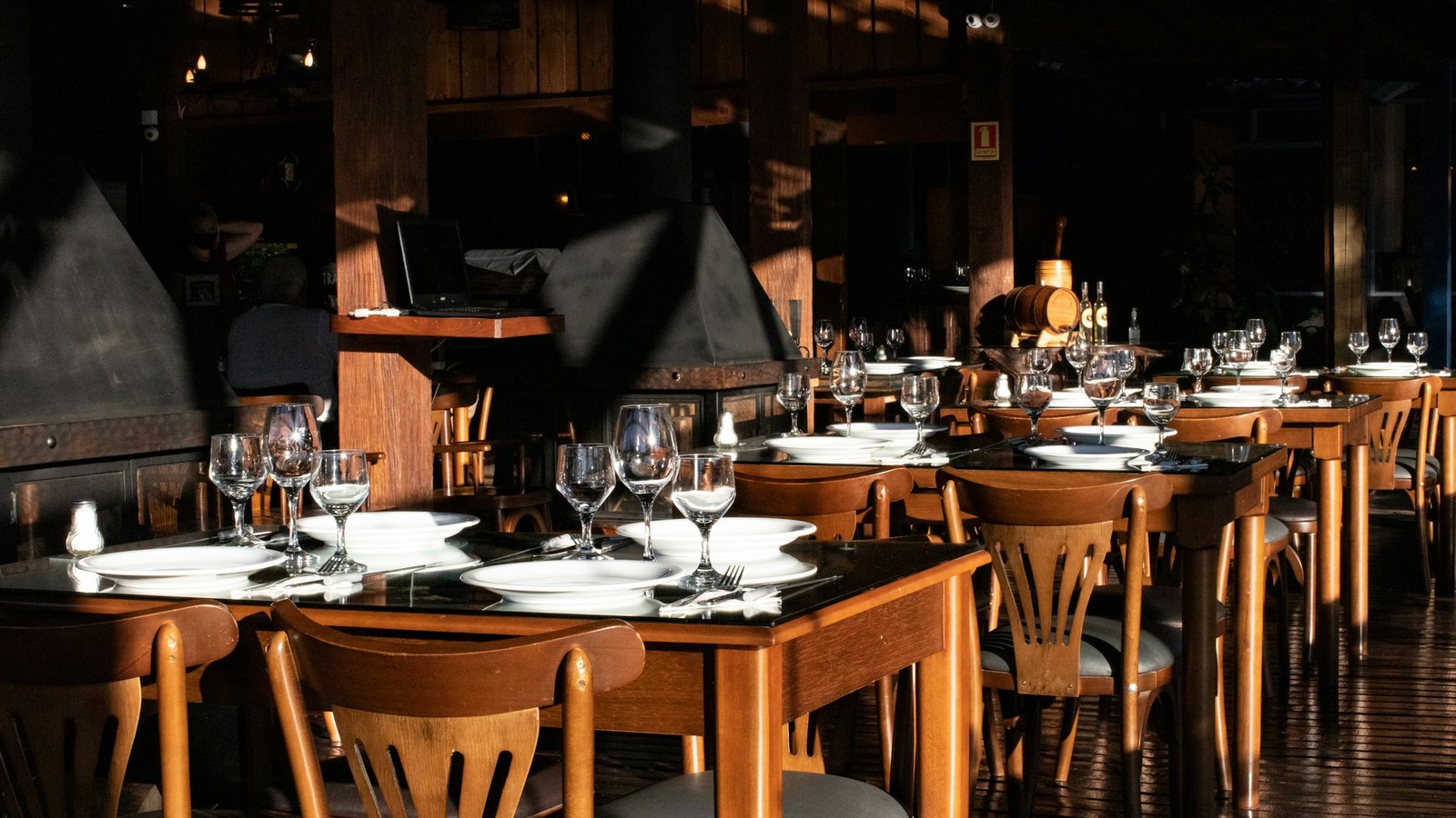 Tables de restaurant dressées avec verres et assiettes, chaises en bois rangées sous les tables
