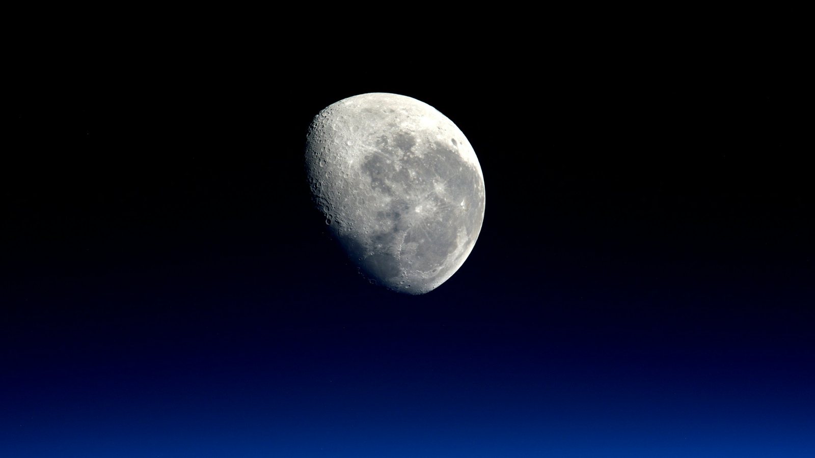 Lune gibbeuse photographiée au téléobjectif dans un ciel qui passe du noir au bleu profond en approchant de l'horizon
