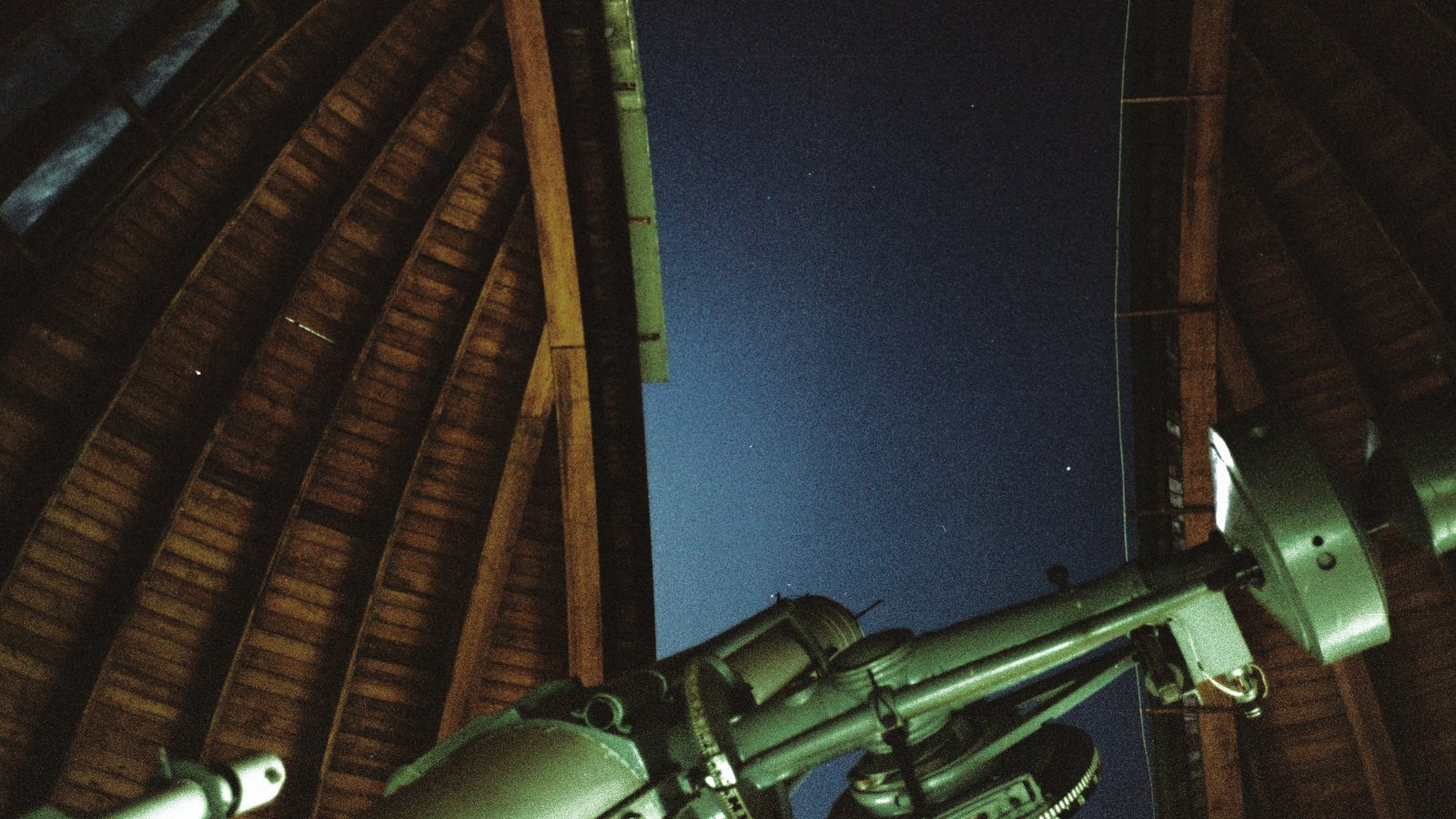Intérieur d'une coupole d'observatoire en bois, la fente ouverte sur un ciel nocturne bleu foncé, avec un grand télescope ancien peint en vert pointé vers l'ouverture